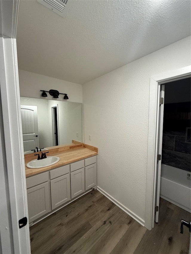 bathroom with vanity, hardwood / wood-style floors, a textured ceiling, and a washtub