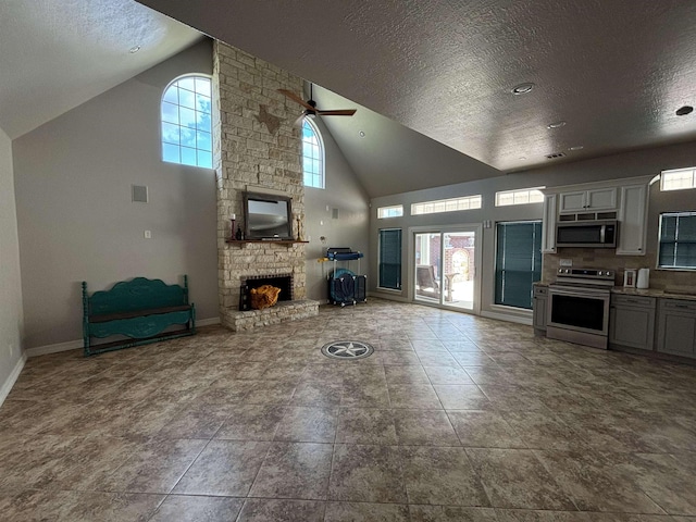 living room featuring a textured ceiling, high vaulted ceiling, a stone fireplace, and ceiling fan