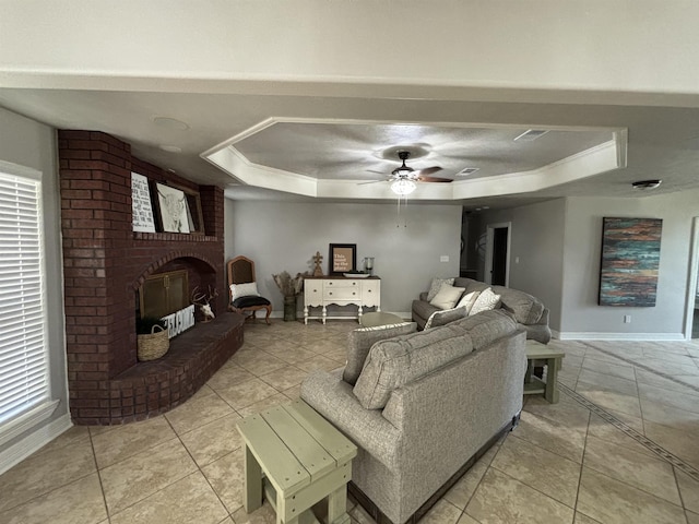 tiled living room with a raised ceiling, ceiling fan, a fireplace, and ornamental molding