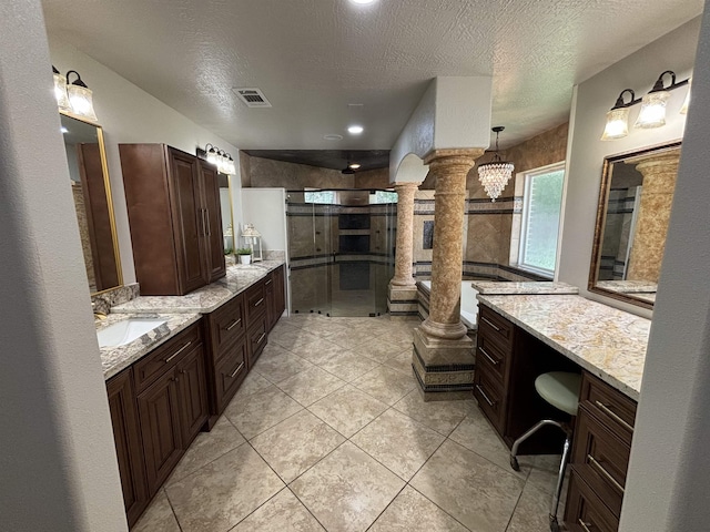 bathroom with an inviting chandelier, decorative columns, a textured ceiling, vanity, and a shower with shower door