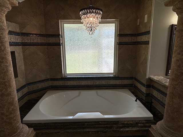 bathroom with a bathing tub, a chandelier, and decorative columns