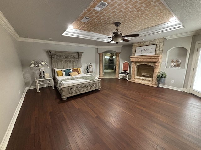 bedroom with ceiling fan, a raised ceiling, a textured ceiling, a fireplace, and ornamental molding