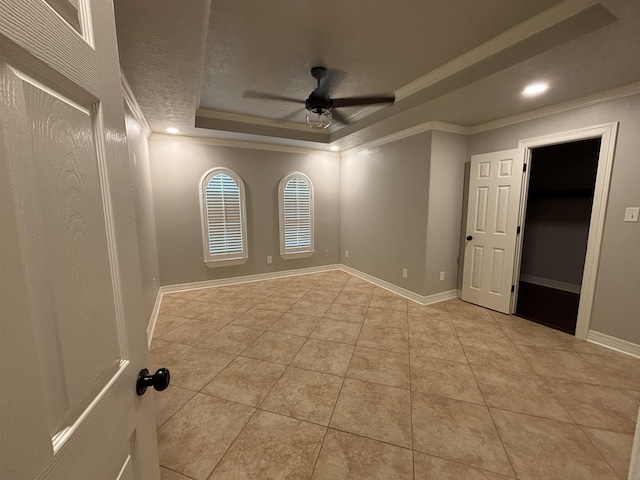 empty room with ornamental molding, a textured ceiling, a tray ceiling, ceiling fan, and light tile patterned floors