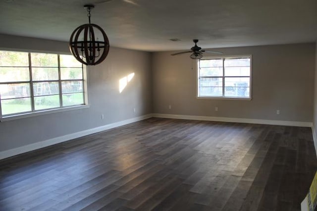 empty room with ceiling fan with notable chandelier and dark hardwood / wood-style flooring