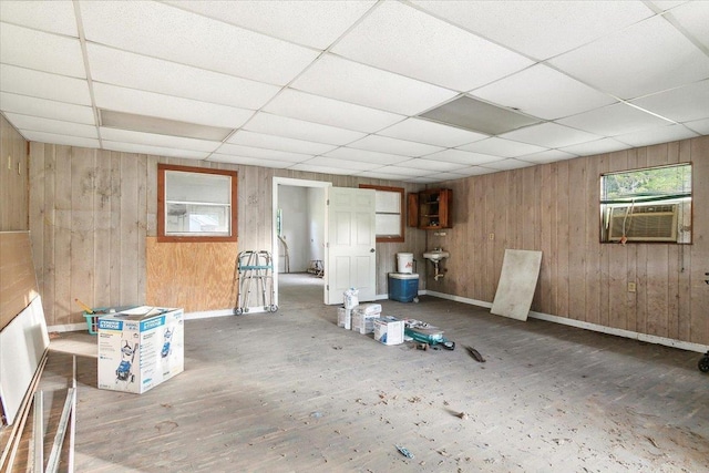 basement with a paneled ceiling, wood walls, and cooling unit