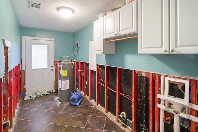 laundry area with a textured ceiling, electric water heater, and dark tile patterned floors