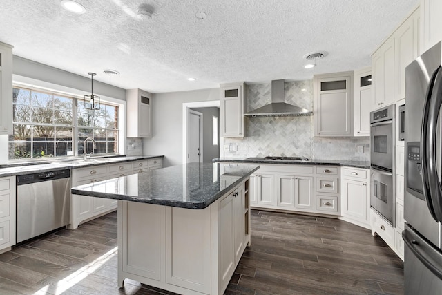 kitchen with a kitchen island, white cabinetry, appliances with stainless steel finishes, and wall chimney range hood