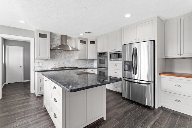 kitchen with a kitchen island, appliances with stainless steel finishes, dark hardwood / wood-style floors, white cabinetry, and wall chimney exhaust hood