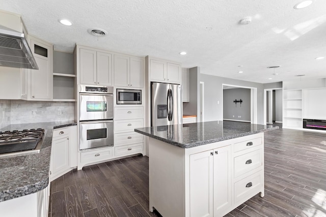 kitchen featuring stainless steel appliances, a center island, wall chimney range hood, and white cabinets