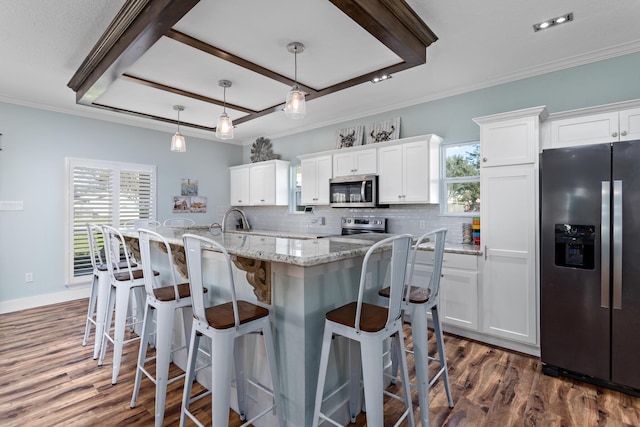 kitchen featuring an island with sink, white cabinets, hanging light fixtures, and appliances with stainless steel finishes