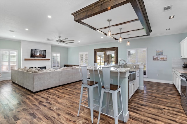 kitchen featuring pendant lighting, white cabinets, light stone countertops, a fireplace, and an island with sink