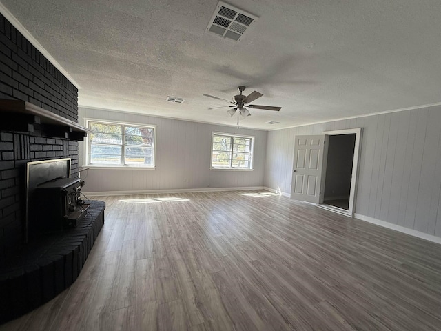 living room with a textured ceiling, a wood stove, wood finished floors, and visible vents
