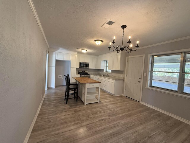kitchen featuring visible vents, butcher block countertops, wood finished floors, stainless steel appliances, and crown molding