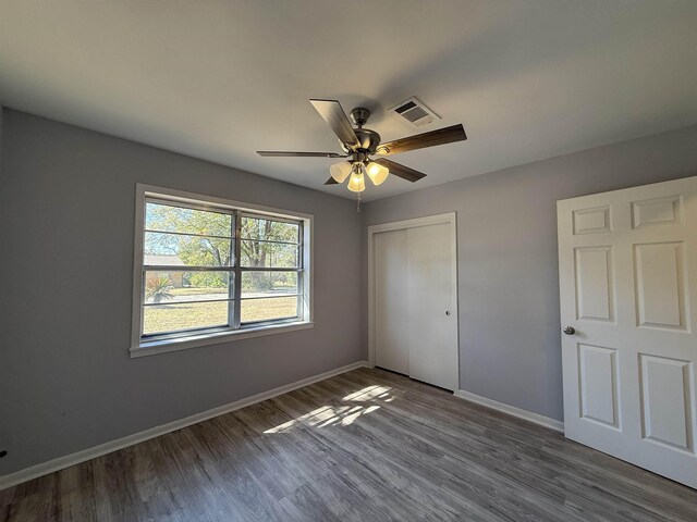 unfurnished bedroom with baseboards, visible vents, ceiling fan, wood finished floors, and a closet