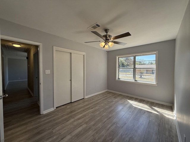 unfurnished bedroom with attic access, baseboards, visible vents, dark wood-type flooring, and a closet