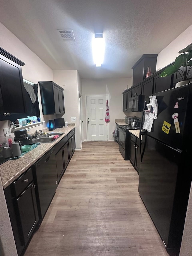 kitchen with sink, black appliances, a textured ceiling, and light hardwood / wood-style flooring