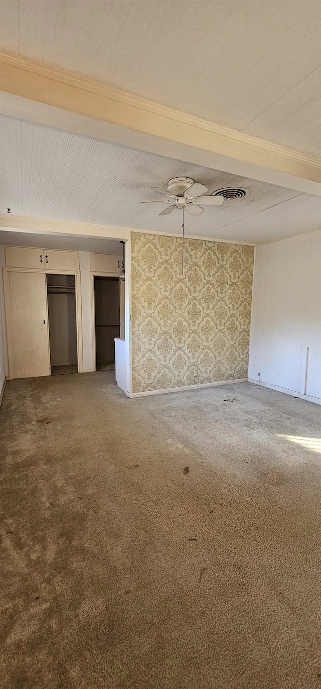 empty room featuring beam ceiling, ceiling fan, and carpet flooring