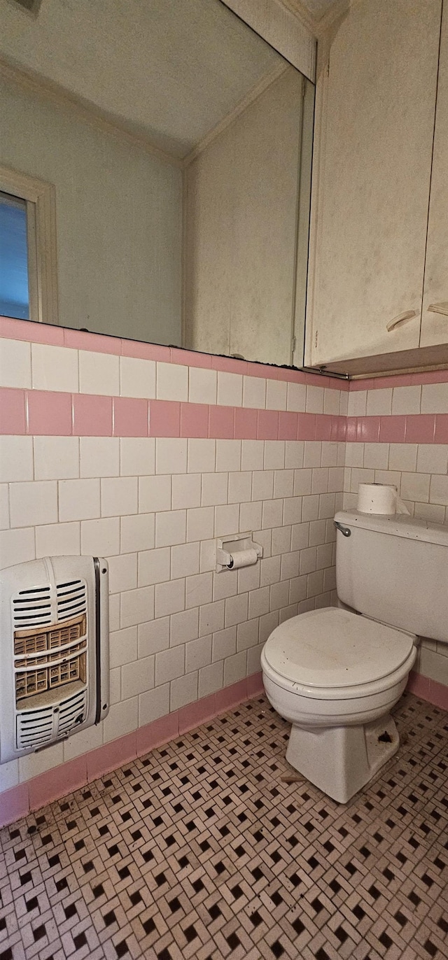 bathroom with heating unit, tile patterned flooring, tile walls, and toilet