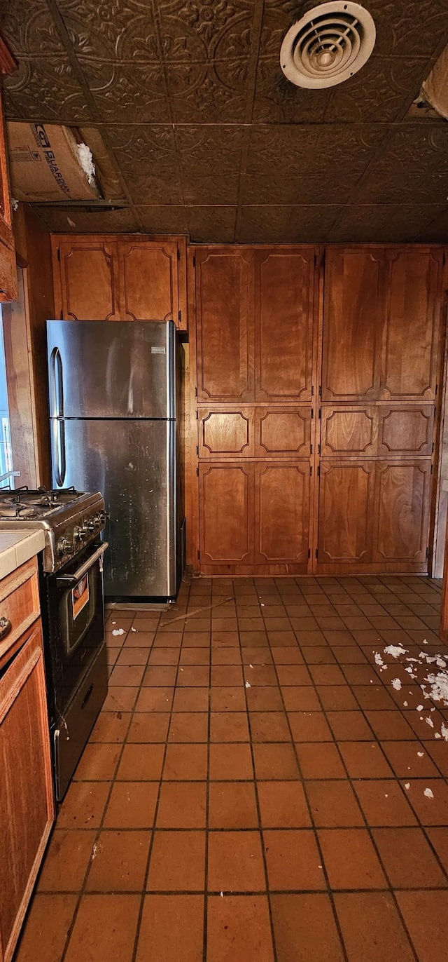 kitchen with stainless steel refrigerator, wooden walls, black range with gas cooktop, and light tile patterned floors