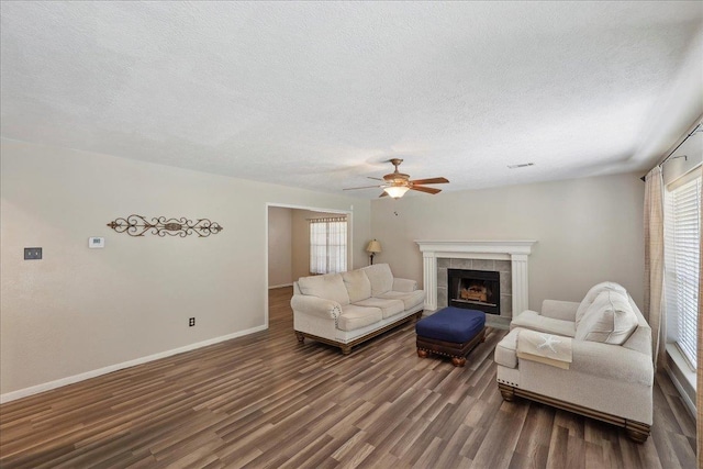 living room with dark wood-style flooring, ceiling fan, a textured ceiling, baseboards, and a fireplace