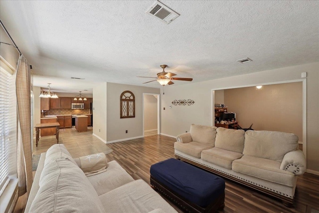 living area with a chandelier, a ceiling fan, a textured ceiling, baseboards, and light wood-type flooring