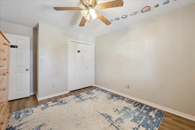 unfurnished bedroom with wood finished floors, baseboards, a closet, and ceiling fan