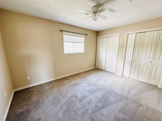 unfurnished bedroom featuring carpet flooring, a textured ceiling, ceiling fan, and multiple closets