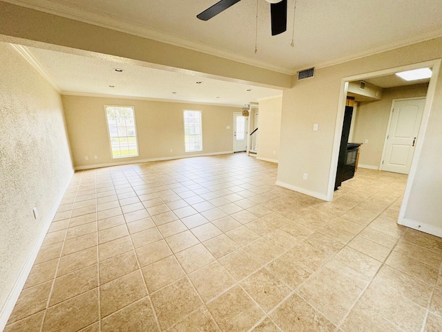 empty room featuring a wood stove, ceiling fan, crown molding, a textured ceiling, and light tile patterned floors