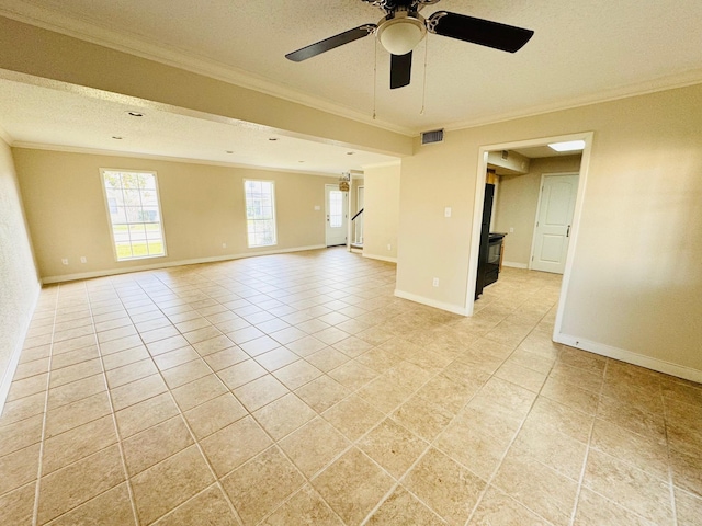 tiled spare room featuring a textured ceiling, a wood stove, ceiling fan, and ornamental molding