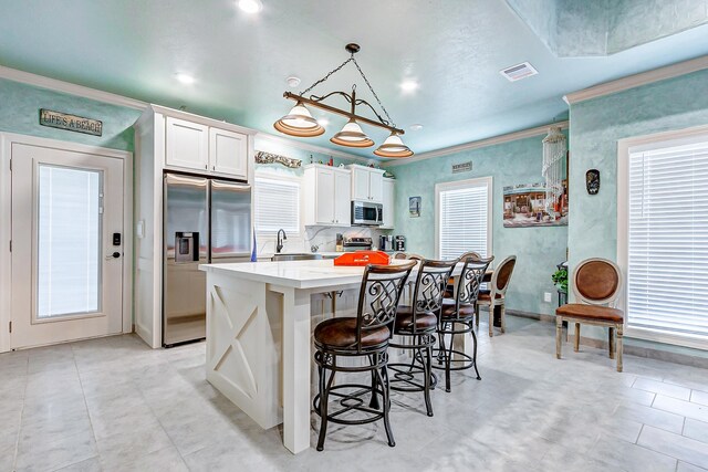 kitchen featuring a kitchen bar, appliances with stainless steel finishes, crown molding, pendant lighting, and white cabinetry