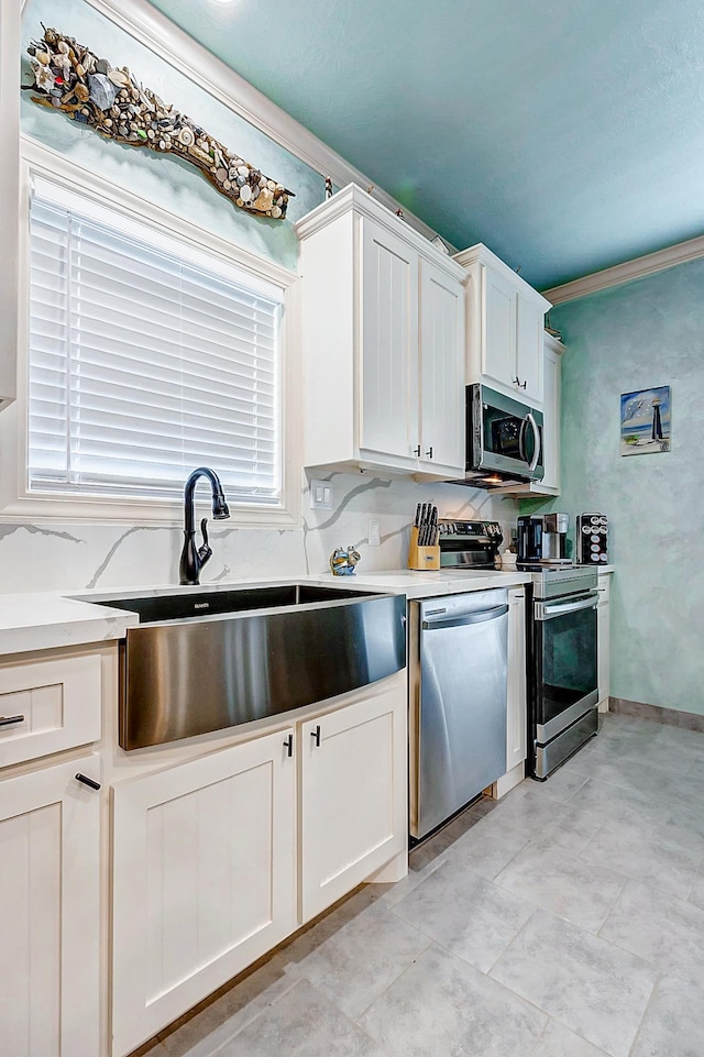 kitchen featuring appliances with stainless steel finishes, white cabinetry, ornamental molding, and sink