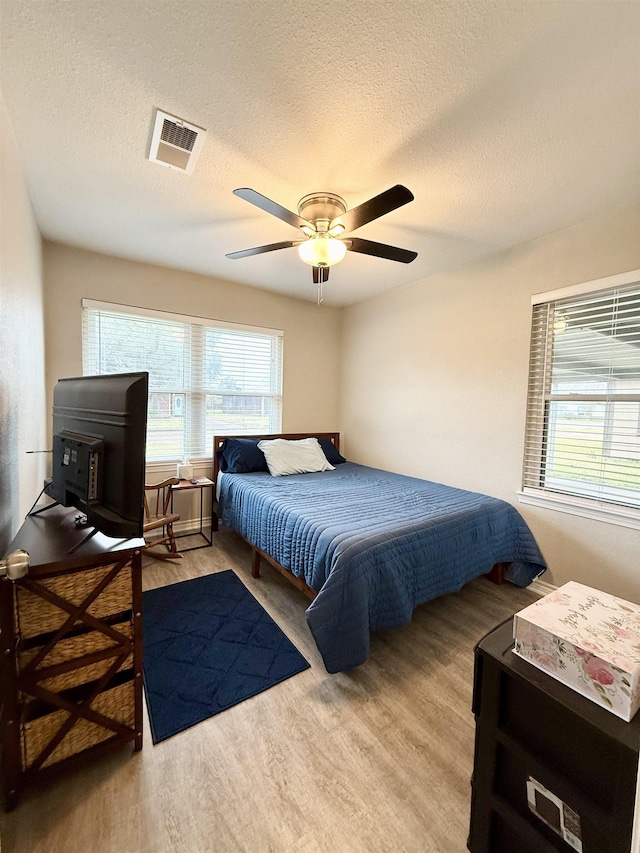 bedroom with ceiling fan, a textured ceiling, and light wood-type flooring