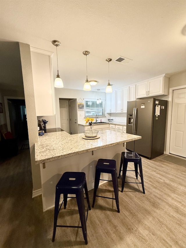 kitchen featuring a breakfast bar, decorative light fixtures, white cabinets, stainless steel fridge, and kitchen peninsula