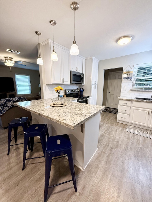 kitchen featuring hanging light fixtures, stainless steel appliances, white cabinets, and a kitchen bar