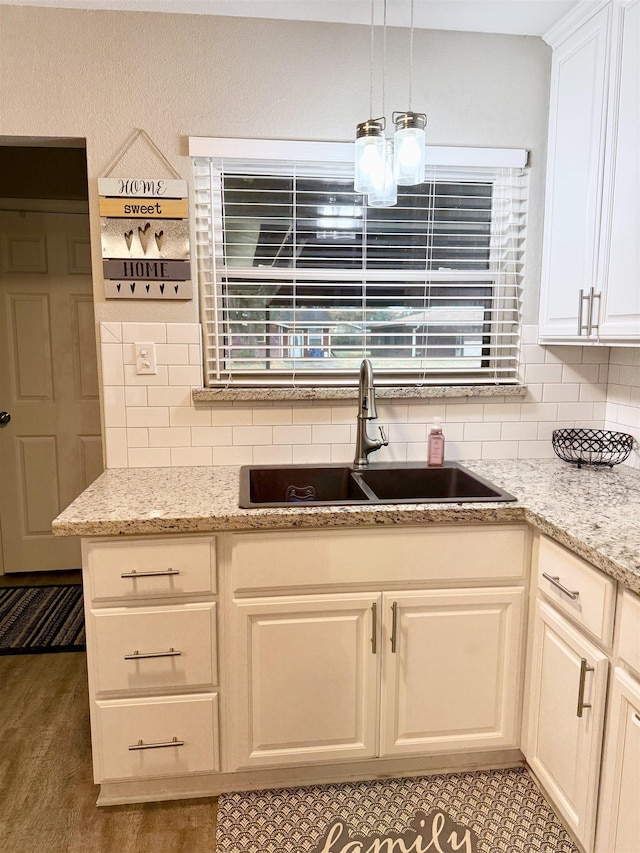 kitchen with tasteful backsplash, sink, light stone counters, and decorative light fixtures