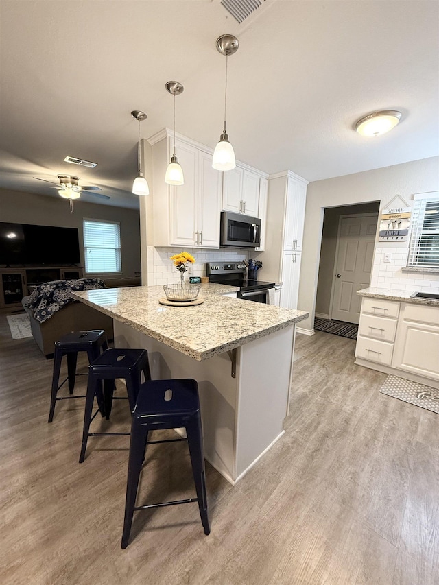 kitchen with appliances with stainless steel finishes, decorative light fixtures, white cabinetry, a kitchen breakfast bar, and light stone countertops