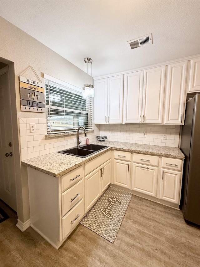 kitchen with sink, black refrigerator, hanging light fixtures, light stone countertops, and light wood-type flooring