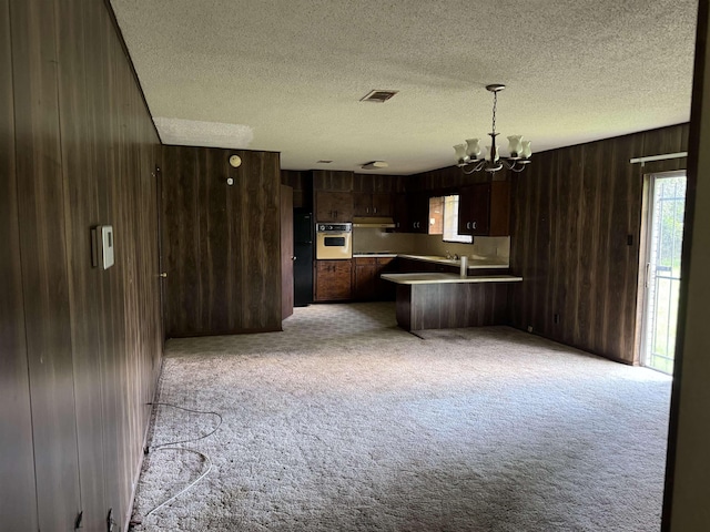 kitchen featuring dark brown cabinetry, hanging light fixtures, kitchen peninsula, oven, and a chandelier