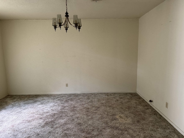 spare room featuring dark carpet and a notable chandelier