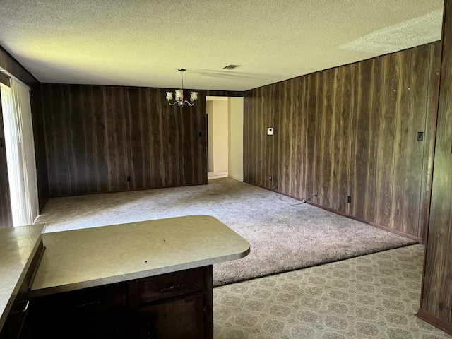 interior space with a textured ceiling, light colored carpet, an inviting chandelier, and wooden walls