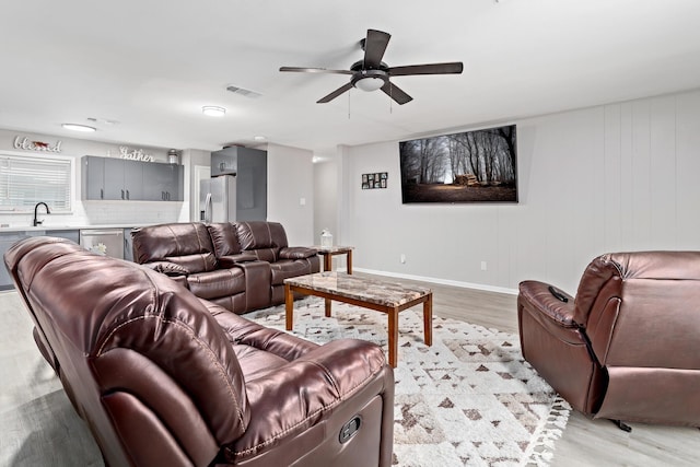 living room with light wood-type flooring, ceiling fan, and sink