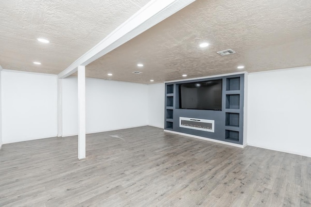 basement with hardwood / wood-style flooring, built in features, and a textured ceiling