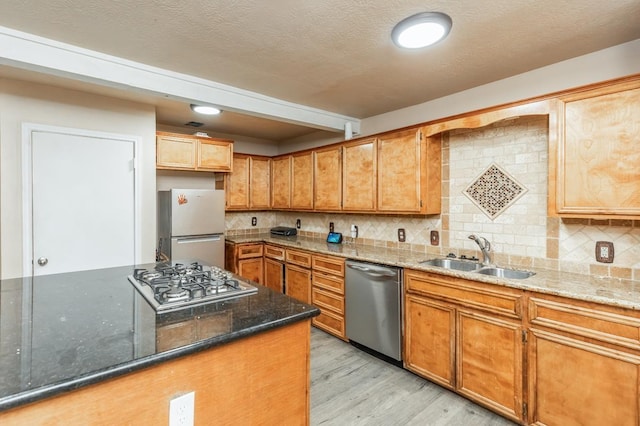 kitchen featuring appliances with stainless steel finishes, backsplash, dark stone counters, sink, and light hardwood / wood-style floors