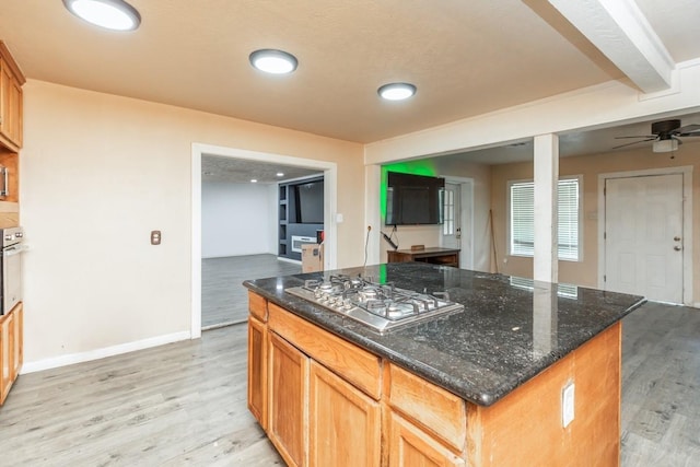 kitchen with light wood-type flooring, ceiling fan, dark stone countertops, a center island, and stainless steel gas stovetop