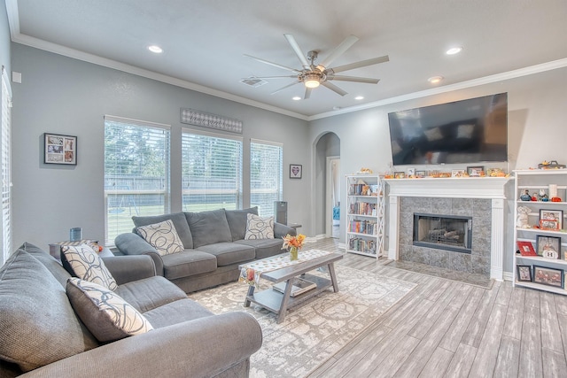 living room featuring ceiling fan, light hardwood / wood-style floors, crown molding, and a fireplace