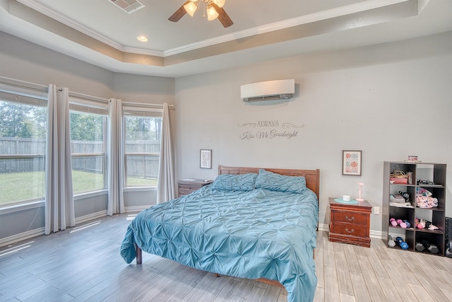 bedroom featuring a wall mounted air conditioner, a raised ceiling, light hardwood / wood-style flooring, ceiling fan, and ornamental molding