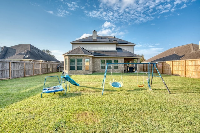 back of house with solar panels, a playground, and a yard