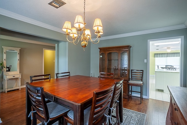 dining area featuring dark wood-style floors, visible vents, an inviting chandelier, and ornamental molding