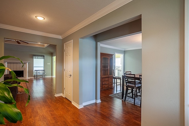 hallway with a textured ceiling, ornamental molding, wood finished floors, and baseboards