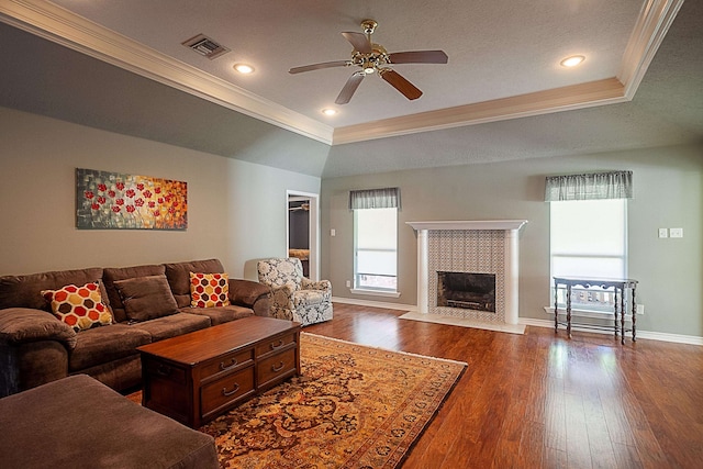 living room featuring baseboards, visible vents, dark wood finished floors, a tray ceiling, and crown molding